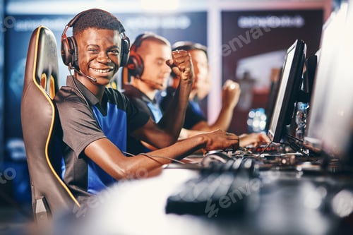 Preview: Side view of a cheerful african guy, professional cybersport gamer wearing headphones looking at