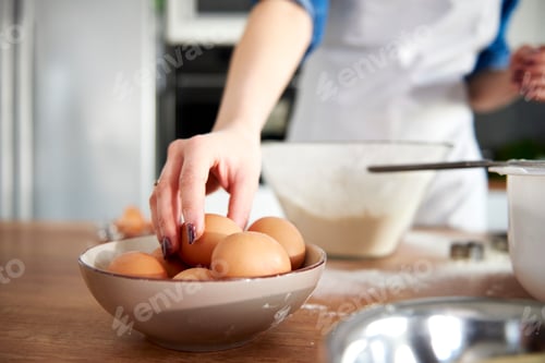 Preview: Woman taking egg from bowl in kitchen