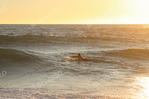 Preview: Back view of male riding on surfboard in sea during sunset