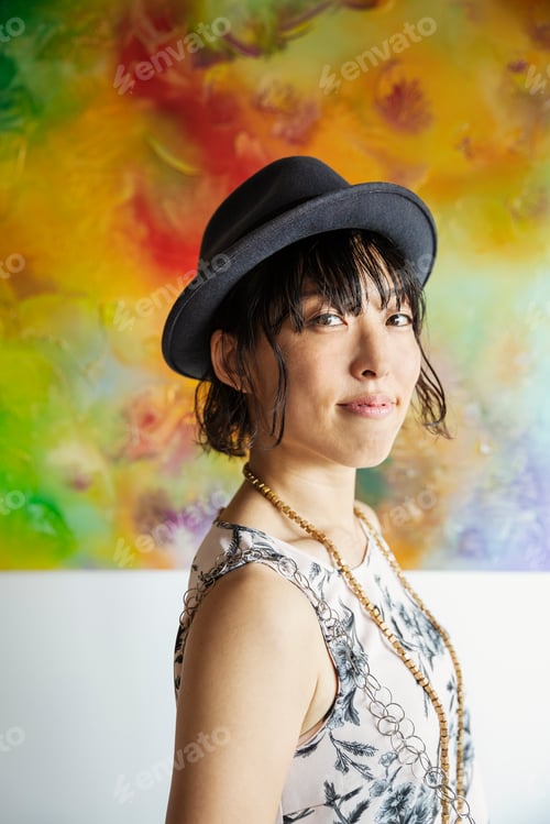 Preview: Japanese woman wearing hat standing in front of abstract painting in an art gallery.