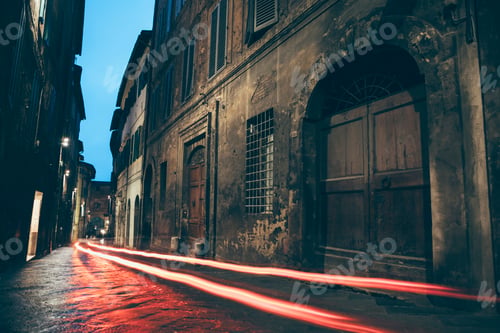 Preview: A city street at night in Siena, long exposure shot with red light trails.