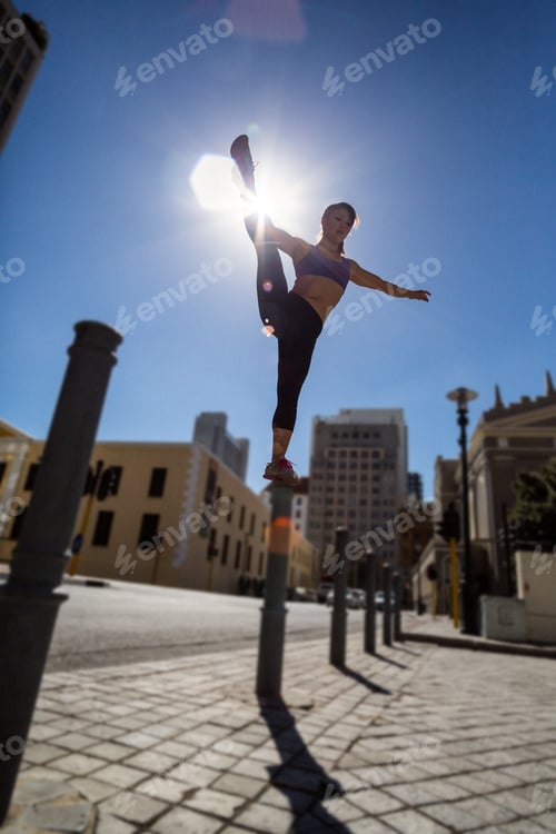 Preview: Athletic woman balancing on bollard and holding her leg in the city