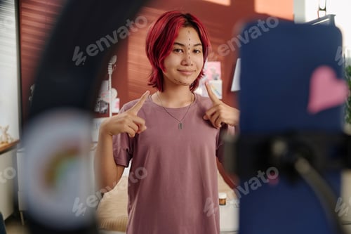 Preview: Happy teenager with liftmarks on face pointing at it during livestream