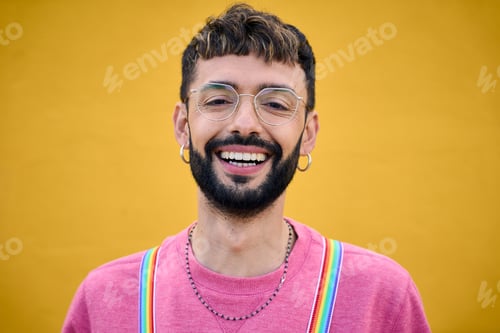 Preview: Close up smiling cheerful young Caucasian man holding his rainbow lgbt suspenders. Generation z.
