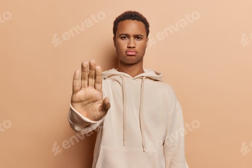 Preview: Stop gesture. Strict displeased young African man raises hand dressed in casual sweatshirt asks not