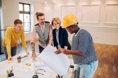 Preview: Multiracial team of architects having a meeting while using blueprints