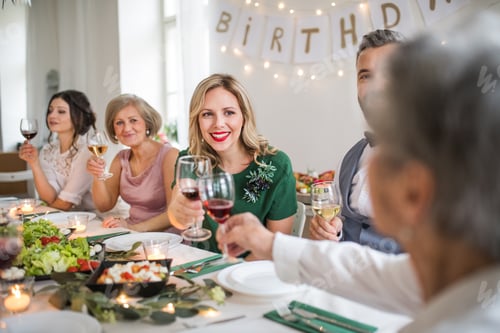 Preview: A big family sitting at a table on a indoor birthday party, clinking glasses.