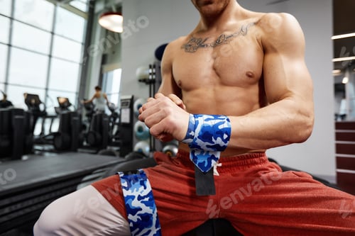 Preview: Young sporty handsome man wraps his arms with gymnastic bandage getting ready for barbell exercises.