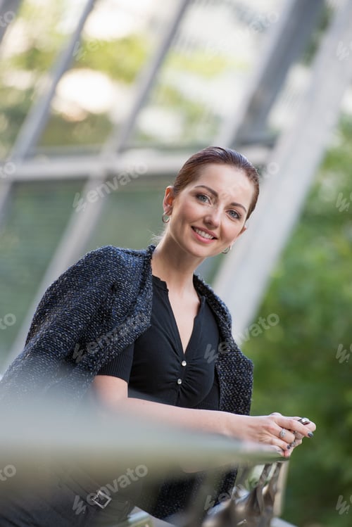 Preview: Business woman in a grey jacket with her hair up, leaning on a railing.