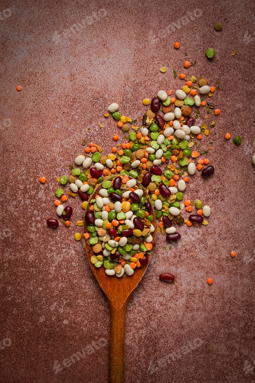 Preview: wooden spoon, with an assortment of legumes, beans, peas, top view, on a brown background,