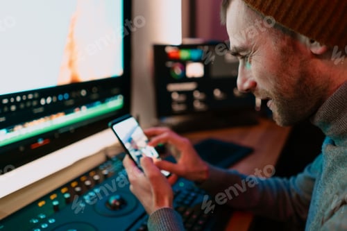 Preview: Male Video Editor sitting at his Computer using phone blank screen