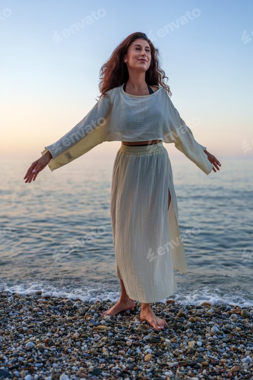 Preview: Carefree woman embracing tranquility, opening arms towards the ocean at sunset