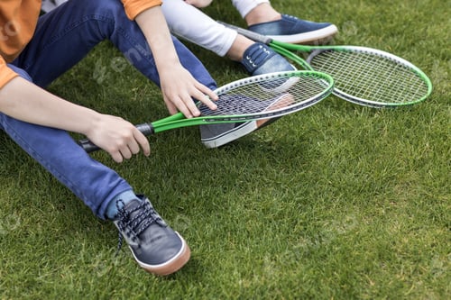 Preview: cropped shot of kids with badminton rackets sitting on green lawn