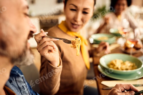 Preview: Close-up of woman feeding her husband with pasta at dining table.