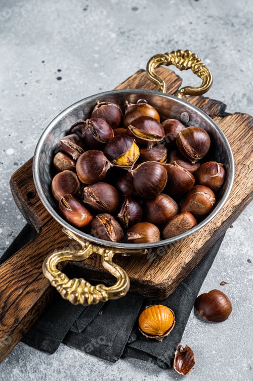 Preview: Cracked roasted chestnuts served in a skillet. Gray background. Top view