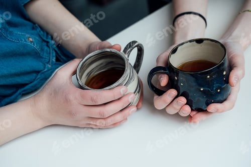 Preview: The hands of two young female ceramics masters hold mugs of tea they have made.