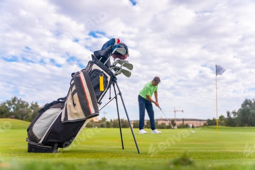 Preview: Caucasian professional golf player on the green preparing for the shot next to the fairway bags