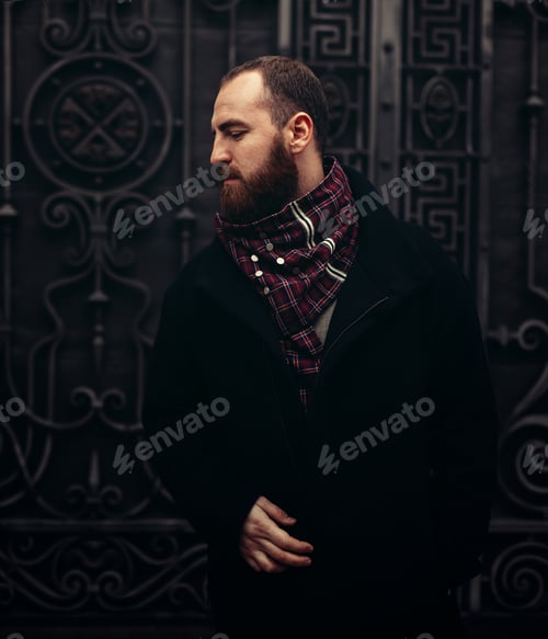 Preview: A handsome brutal man with a beard on the street. Autumn collection. Black coat and checkered scarf