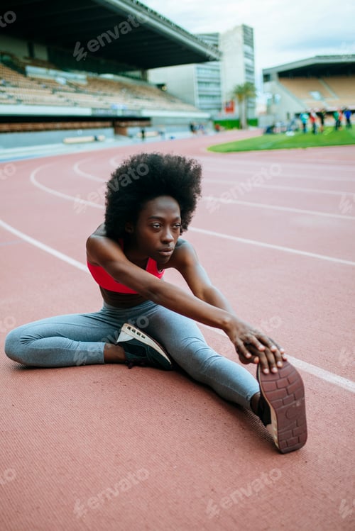 Preview: Young female athlete stretching on running track in stadium