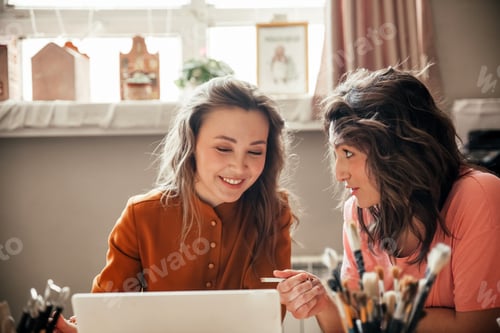 Preview: Two young female entrepreneurs sit with laptop in their workshop
