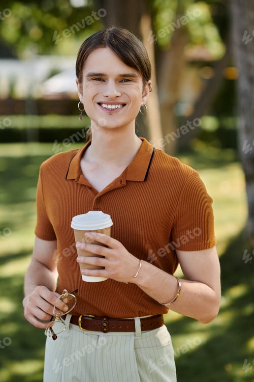 Preview: A cheerful non binary individual enjoys coffee while standing outside in an office setting