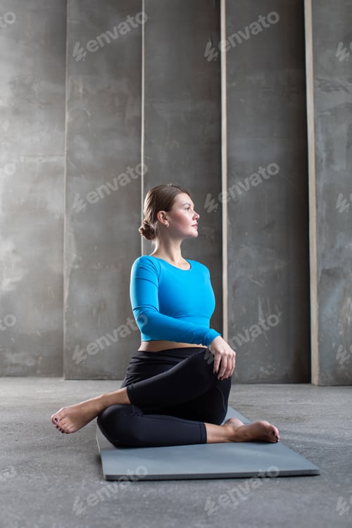 Preview: A woman in sportswear does a back twist while sitting on a yoga mat. Pilates, a healthy back class.