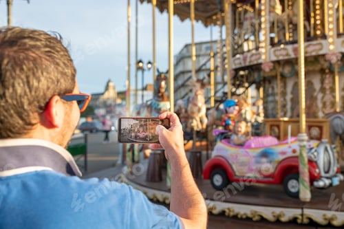 Preview: Father takes photos or videos of his daughter on the carousel on the phone