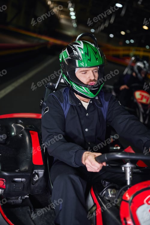 Preview: focused man in sportswear and helmet driving sport car for karting on indoor circuit, hobby