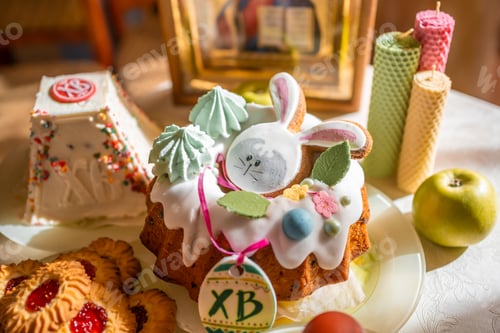Preview: Easter cake with painted eggs, apples and cookies on table in home kitchen. Church icons and candle