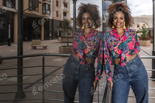 Preview: Happy ethnic woman in trendy wear standing near glass wall