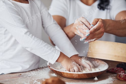 Preview: Close up view of woman with her granddaughter preparing food with flour on kitchen