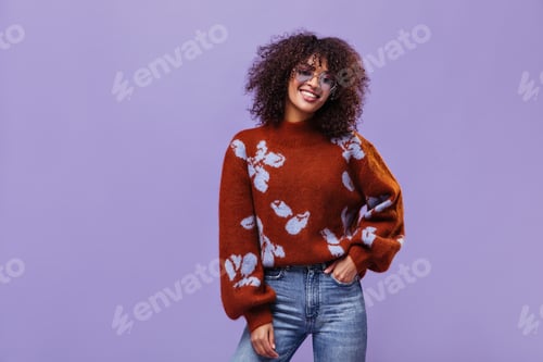 Preview: Joyful woman in jeans, warm sweater and sunglasses smiles on purple background. Pretty girl smiles