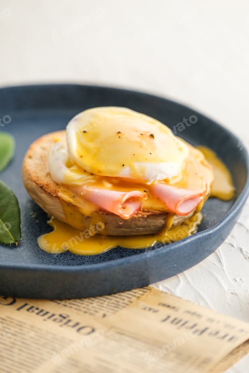 Preview: egg Benedict with hollandaise sauce on blue plate on table in white kitchen