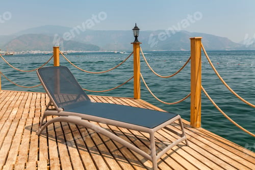 Preview: Sunbed on the wooden pier on the background of mountains and the sea port.
