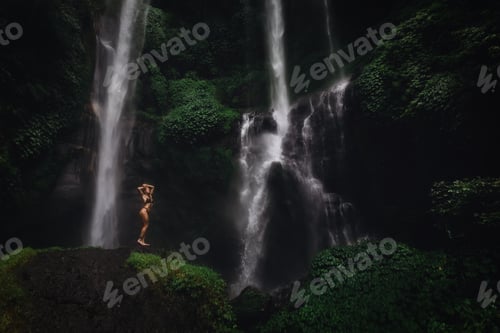 Preview: Beautiful young woman in bikini relaxing in front of waterfall. Ecotourism concept image travel girl