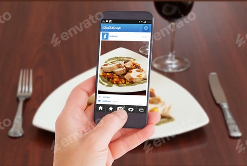 Preview: Female Hand Holding A Smartphone Against High Angle View Of Delicious Chicken Dish With Salsa
