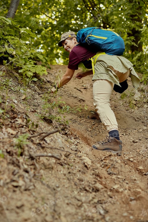 Preview: Below view of happy woman climbing up dusty forest trail while hiking in nature.