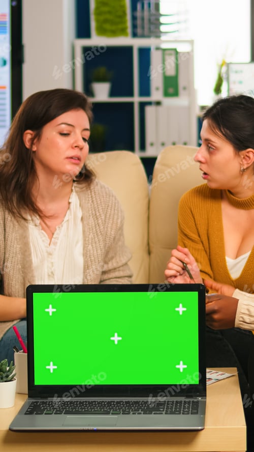 Preview: Businesswomen discussing in back of laptop with greenscreen