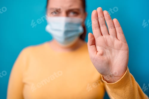 Preview: Closeup image of caucasian woman outstretched hand and showing stop hand sign on a blue background.