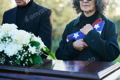 Preview: Cropped shot of mature grey haired mourning woman holding folded US flag