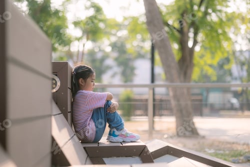 Preview: A little girl sits on a bench in a park