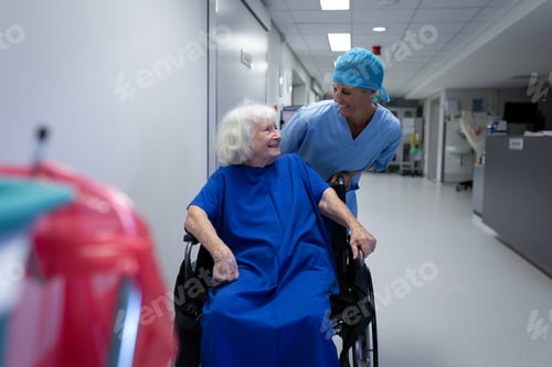 Preview: Female surgeon talking with senior female patient sitting in a wheelchair in hospital corridor