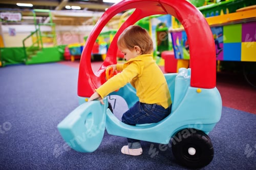 Preview: Cute baby girl rides on a plastic car in indoor play center.