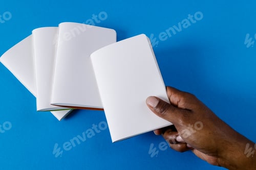 Preview: Hand of biracial man holding notebook over notebooks with copy space on blue background
