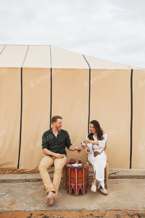 Preview: Young happy couple enjoying traditional moroccan mint tea in glamping camp in Sahara desert, Morocco