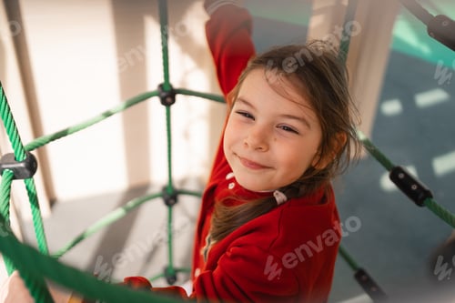 Preview: Close-up of a smiling child on a rope net at a park, embodying playful moments and happiness