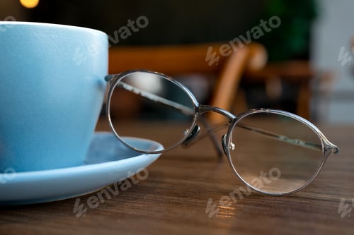 Preview: Coffee in blue cup on wooden table in cafe with reading glasses