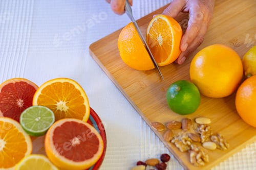Preview: Group of whole and halved citrus fruits, wooden cutting board with female hand cutting an orange