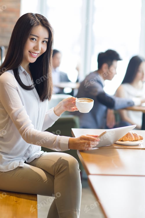 Preview: Young woman using digital tablet in café