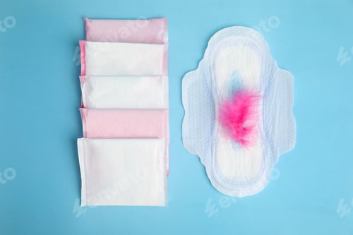Preview: Menstrual pads and pink feather on light blue background, flat lay